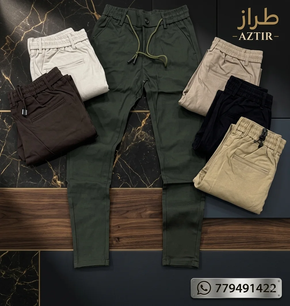 Six folded men's drawstring pants in various earth tones displayed on marble and wood surfaces