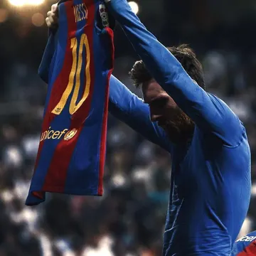 Footballer holding up a blue and red striped jersey with 'MESSI' and number '10' in gold