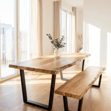A wooden dining table and bench with black metal legs in a bright modern room with large windows
