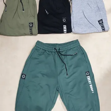 Four pairs of drawstring sweatpants in olive black gray and teal laid flat on a light beige surface