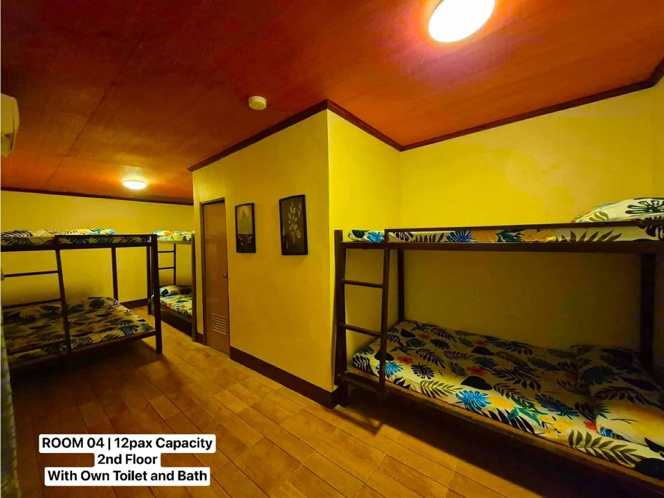 Dorm room with wooden floors and ceilings featuring multiple bunk beds with tropical patterned bedding