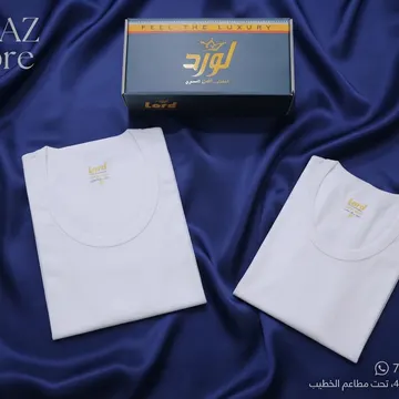 Two white folded t-shirts with gold logos on blue satin fabric with branded packaging nearby