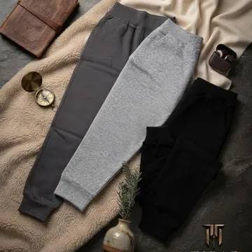 Three joggers in gray black and heather gray on a beige fleece blanket with accessories