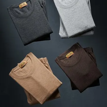 Four folded TIRAZ brand crewneck shirts in gray brown and tan floating in a dark studio setting