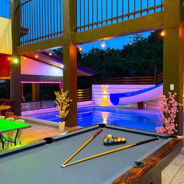 Pool table beside a lit pool with slide at dusk