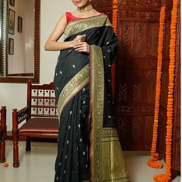 Woman wearing black and gold embroidered saree with red blouse standing near wooden screen with marigold garlands