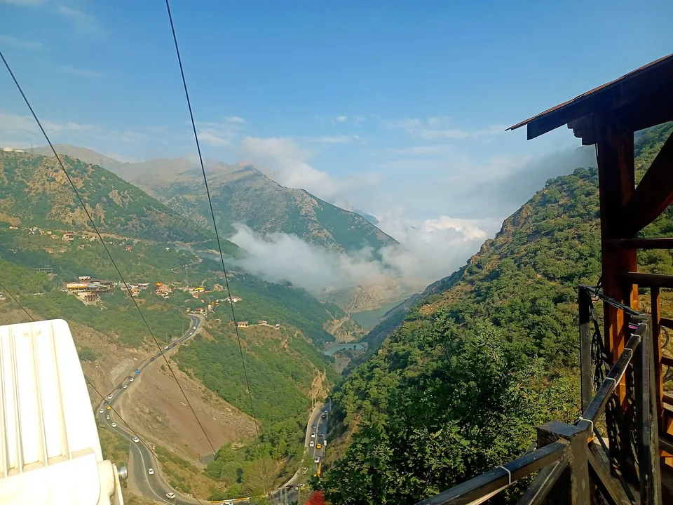 Cable car overlooks mountain valley with winding road clouds and lake