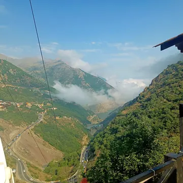 Cable car overlooks mountain valley with winding road clouds and lake