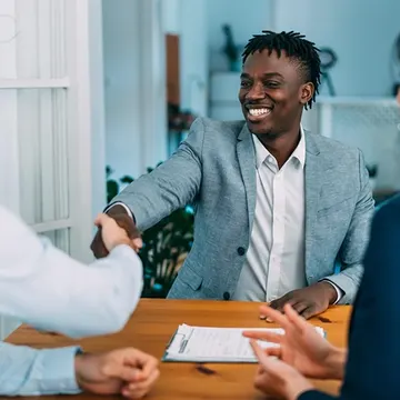 Three people in business attire shaking hands over a wooden table with documents