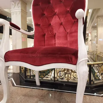 Red velvet tufted chair with white frame in a luxurious marble lobby with gold railings
