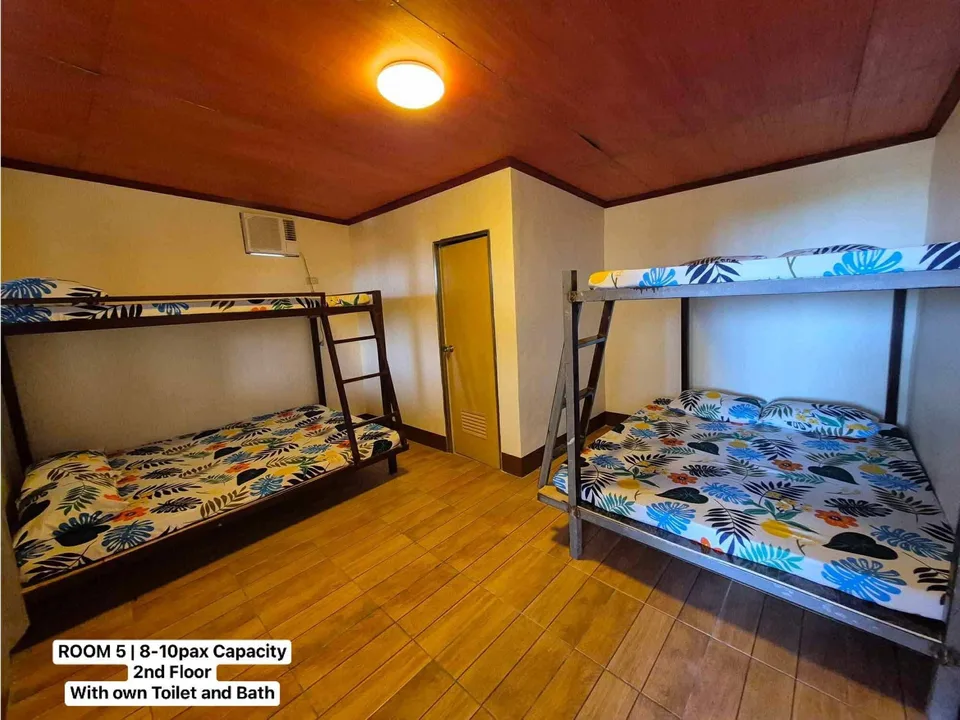 Two metal bunk beds with tropical leaf sheets in a wooden-floored guest room with yellow walls and ceiling light