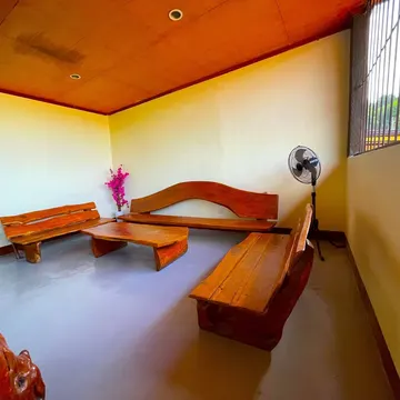 A room with wooden benches and table, a standing fan, and a pink flower vase near a window