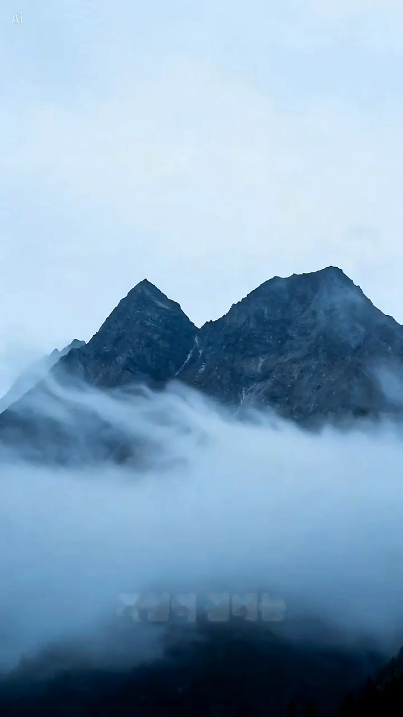 A mountain peak emerges from a thick layer of clouds under an overcast sky, with a faint watermark visible in the lower portion