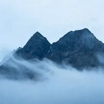 A mountain peak emerges from a thick layer of clouds under an overcast sky, with a faint watermark visible in the lower portion