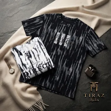 Two tie-dye t-shirts with text print on beige scarf with watch and earbuds on stone surface