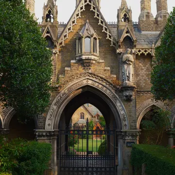 Gothic stone archway with statue and gate leading to a garden path