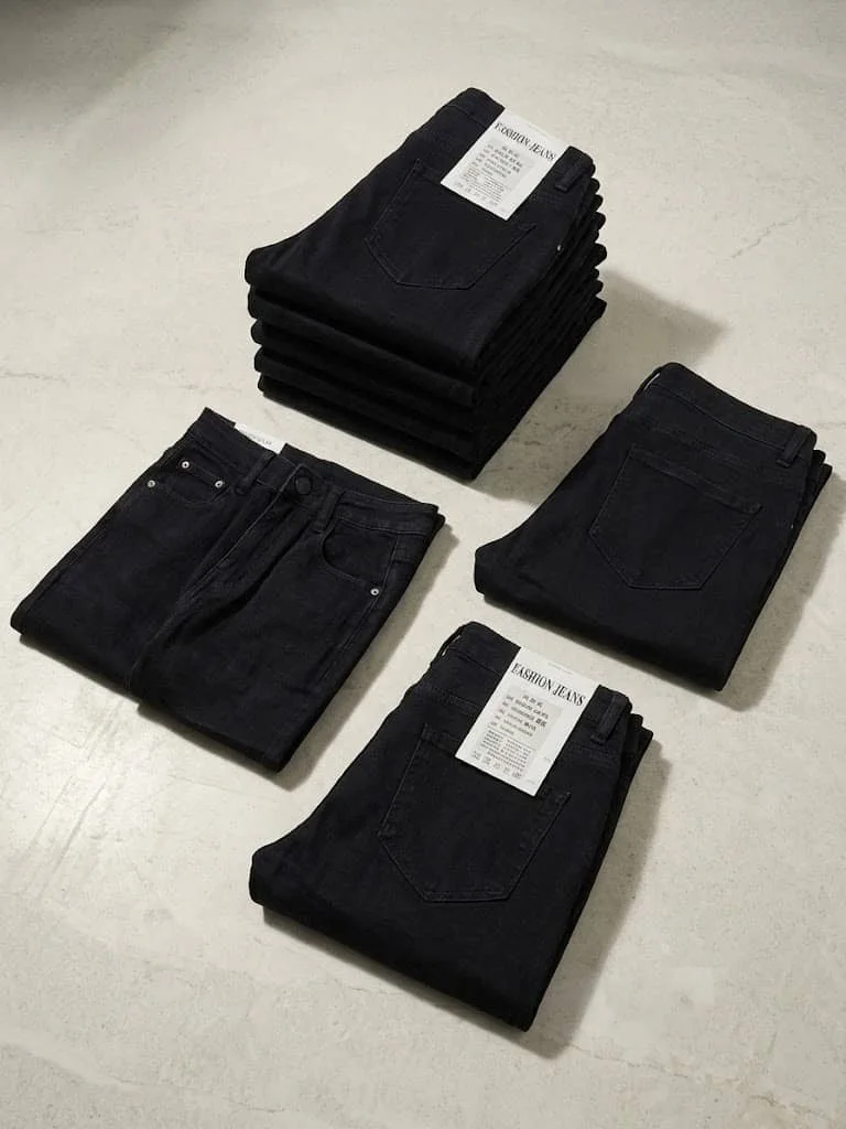 Neatly folded dark jeans with tags on a gray concrete surface