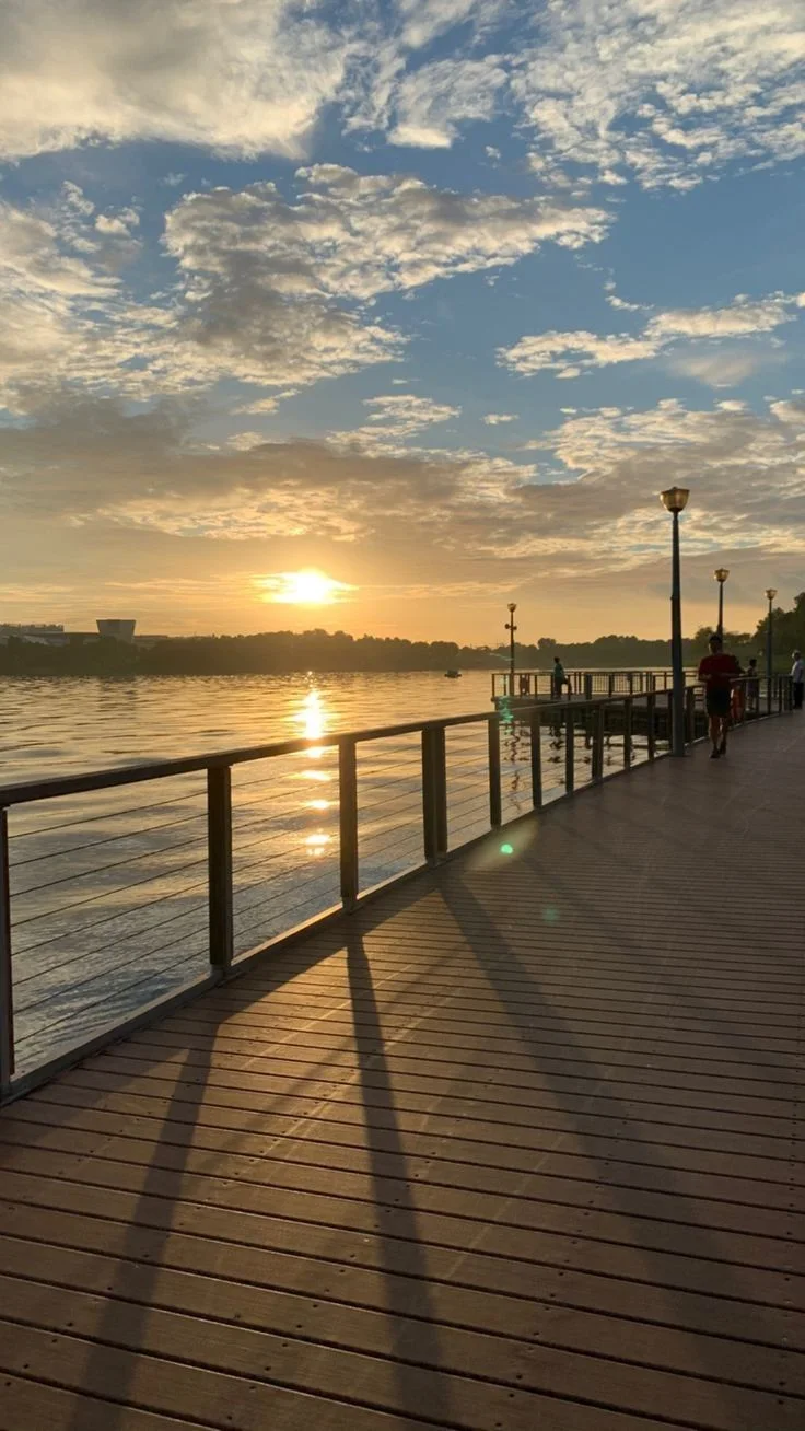 Sunset over a wooden boardwalk with people walking and water reflecting golden light