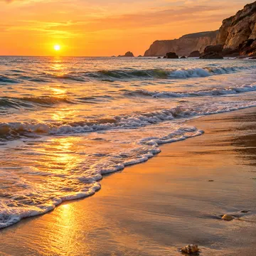 Sunset waves washing over sandy beach with seashells near cliffs