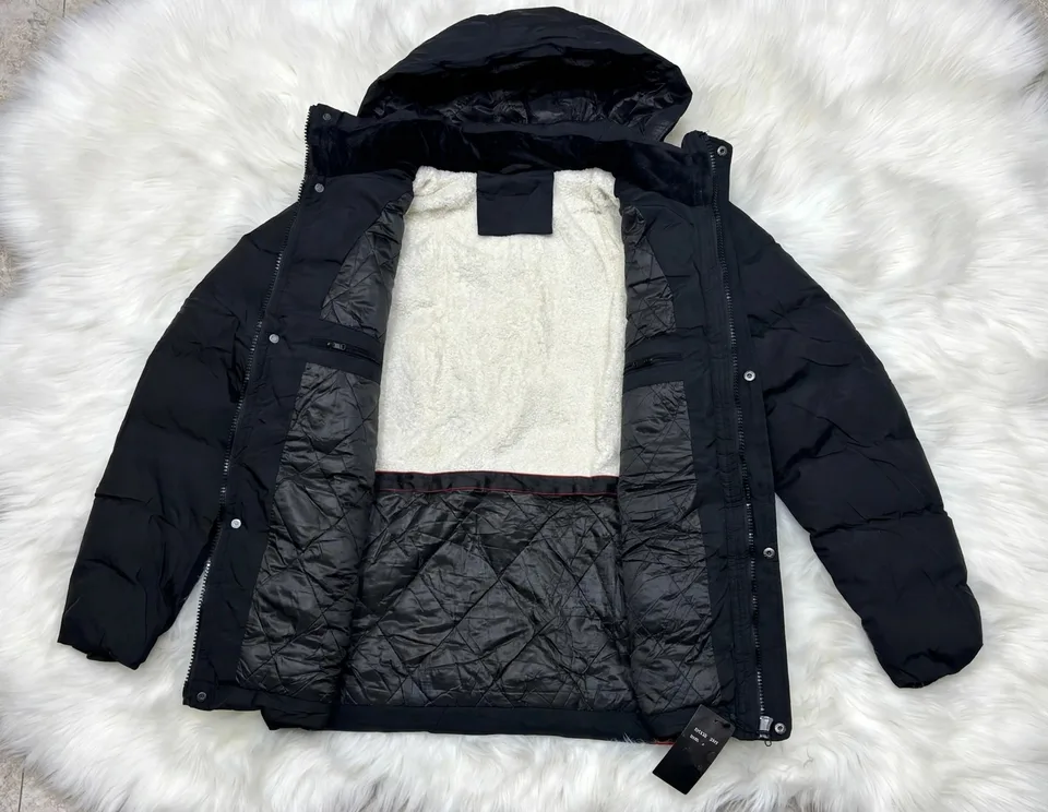 A black puffer jacket with a white fleece lining is laid open on a white fluffy rug, showing its quilted interior and zipper details