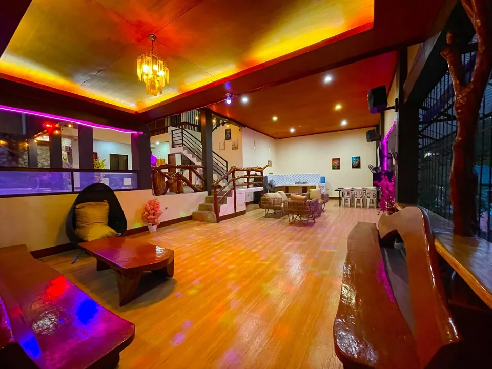 A warmly lit indoor lounge with wooden floors glowing under colorful disco lights and eclectic furniture