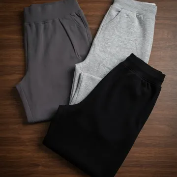 Three folded sweatpants in charcoal gray heather gray and black on a wooden surface