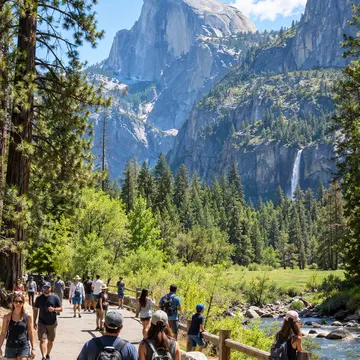 People hiking on a trail near a river with Half Dome and waterfall in background