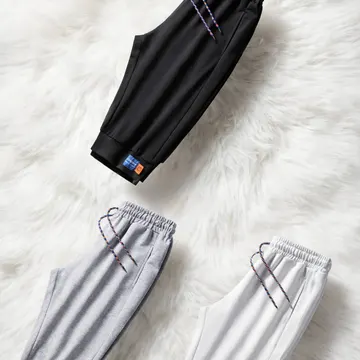Three colorway joggers with colorful drawstrings on a fluffy white rug under a crown logo