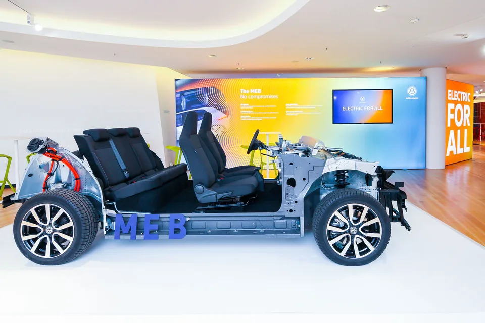 Exposed Volkswagen MEB electric vehicle chassis with black seats and orange wiring on display