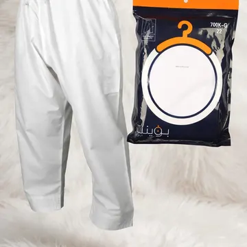 A pair of white pants and a packaged hanger are displayed on a white furry surface, with a gold plaque reading 'TIRAZ STORE' in front