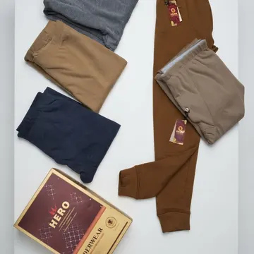 Five folded men's thermal underwear pants and a HERO underwear box on a white surface