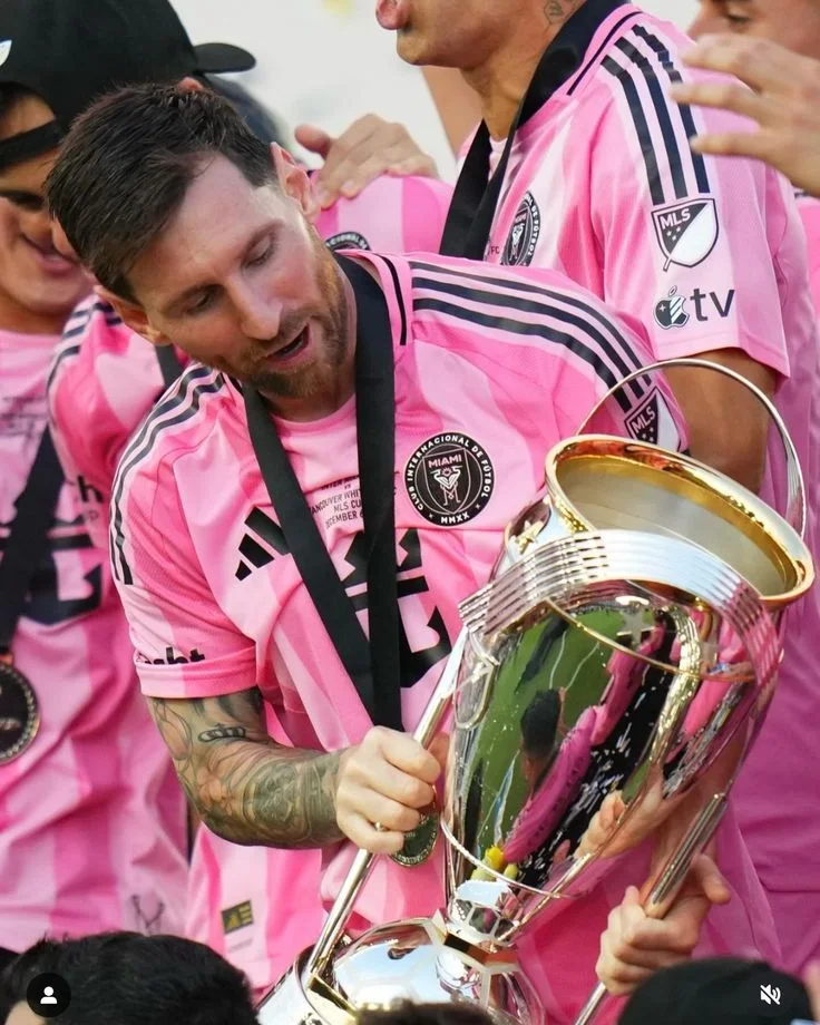 Lionel Messi holding a silver trophy with teammates in pink jerseys celebrating