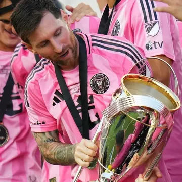 Lionel Messi holding a silver trophy with teammates in pink jerseys celebrating