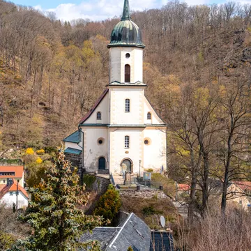 White church with green dome on hillside surrounded by autumn trees and village rooftops