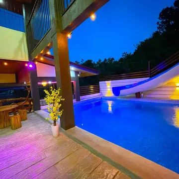 A lit pool area at dusk with a slide and wooden seating under string lights