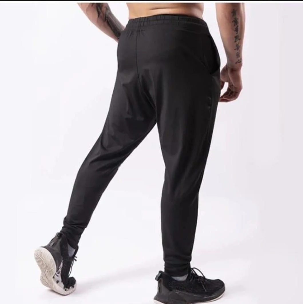 Person wearing black joggers and sneakers with tattoos on arms standing in studio